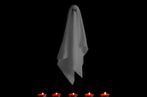 folha de fantasma branco voando em fundo escuro com velas vermelhas. conceito assustador de halloween. foto