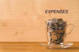 moedas em um copo com texto de despesas na mesa de madeira. conceito financeiro. espaço livre para texto foto