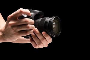 mão masculina segurando uma câmera digital em um fundo preto. foto