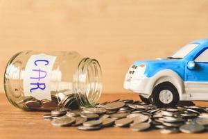moedas saindo de uma jarra de vidro com etiqueta de carro e brinquedo de carro na mesa de madeira. conceito financeiro foto