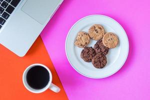 biscoitos com xícara de café e laptop em fundo colorido. foto