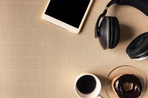 vista superior de fones de ouvido com tablet, xícara de café e rosquinha na mesa. espaço livre para texto foto