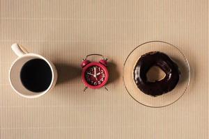 vista superior da xícara de café com donut e relógio na mesa. foto