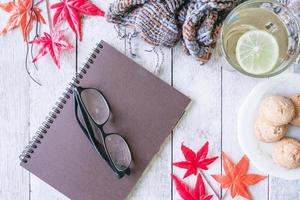 xícara de chá com limão, biscoito, cachecol, notebook, óculos e maple folhas na mesa de madeira. foto