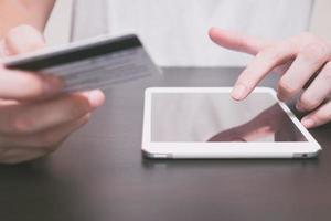 close-up de mãos masculinas usando tablet e segurando o cartão de crédito em cima da mesa, conceito de compras online. foto