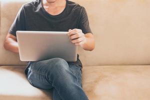 close-up de casual jovem sentado no sofá e usando um laptop em casa. foto