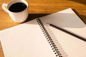 caderno em branco com lápis e xícara de café no fundo da mesa de madeira. foto