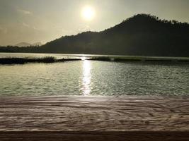 tampo da mesa de madeira, nascer do sol de fundo no lago foto