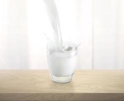 derramando leite em copo de vidro com salpicos, na mesa de madeira foto