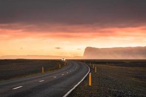 estrada de asfalto curva cênica com condução de carro e céu pôr do sol na montanha na islândia foto