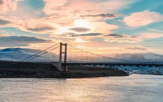 belo pôr do sol sobre a ponte pênsil na lagoa do rio glacial jokulsarlon com iceberg flutuando no sul do parque nacional vatnajokull na islândia foto