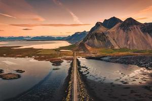 belo nascer do sol sobre a montanha vestrahorn com estrada para a praia de areia preta no oceano atlântico em stokksnes no sudeste da islândia foto