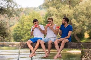 homens desfrutando de melancia enquanto está sentado na ponte de madeira foto