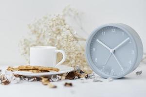 xícara de café e despertador clássico em uma mesa branca. foto