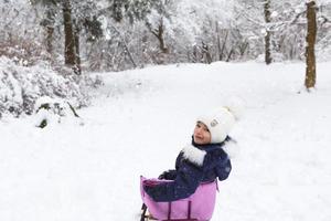 uma menina com roupas quentes está sentada em um trenó. floresta de inverno, caminhada foto