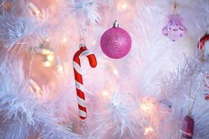 decorações de natal em uma árvore de natal artificial branca, um balão rosa e a bengala listrada de doces do papai noel. ano novo, fundo festivo. espaço para texto foto