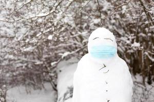 boneco de neve em uma máscara médica - uma nova realidade, proteção contra doenças, infecções, vida na epidemia de covid. as mãos das mulheres colocam uma máscara de boneco de neve. atividades ao ar livre em família de inverno foto