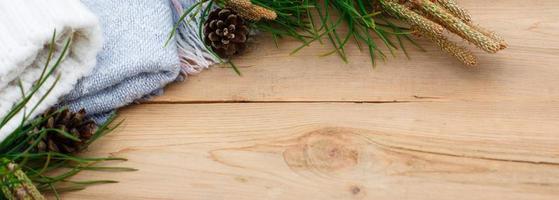 flatlay de natal em um fundo de madeira rústico agulhas de pinheiro verde com cones, coisas de lã quentes em branco e azul. conceito de ano novo, conforto em casa de férias de inverno. espaço para texto foto