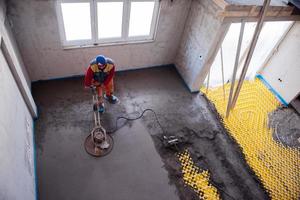 trabalhador realizando e polindo piso de betonilha de areia e cimento foto