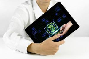 empresário segurando um tablet com símbolo de bitcoin e ícones de laptop em fundo binário foto