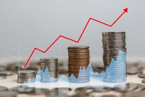 negócios finanças investimentos economia economizando dinheiro pilha moeda inflação e seta vermelha com tela virtual do gráfico na mesa. foto