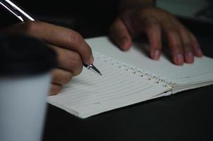 mão de homem segurando a caneta escrever o diário de nota no livro. foto