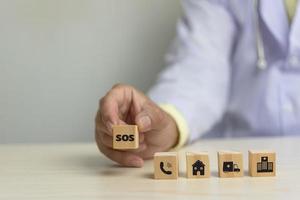 médico segurando o conceito de negócio de cuidados de saúde de ícone de bloco de cubo de madeira sos na mesa. foto