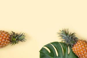 lindo abacaxi em folhas tropicais de palmeira monstera isoladas em fundo amarelo alaranjado pastel brilhante, vista superior, postura plana, sobrecarga acima das frutas de verão. foto