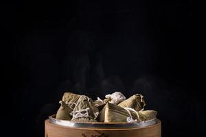 bolinho de arroz, zongzi - bando de comida tradicional chinesa cozida na mesa de madeira sobre fundo preto, conceito de festival de barco dragão, close-up, copie o espaço foto