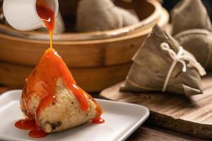 comendo zongzi - bolinho de arroz do festival do barco dragão jovem asiática comendo comida tradicional chinesa na mesa de madeira em casa celebração, close-up