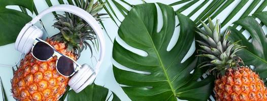 abacaxi engraçado usando fone de ouvido branco, conceito de ouvir música, isolado em fundo colorido com folhas de palmeira tropical, vista superior, design plano leigo. foto