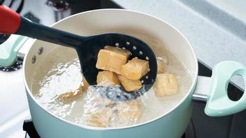 cozinhar tofu seco em cubos em cubos no fogão a gás na cozinha de casa, estilo de vida, closeup. foto