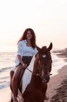 mulher com roupas de verão gosta de andar a cavalo em uma bela praia ao pôr do sol. foco seletivo foto