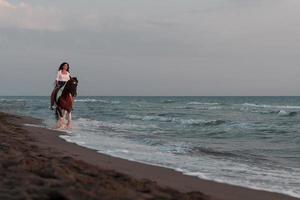 mulher com roupas de verão gosta de andar a cavalo em uma bela praia ao pôr do sol. foco seletivo foto