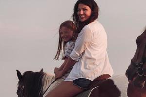 a família passa o tempo com seus filhos enquanto andam a cavalo juntos em uma bela praia de areia ao pôr do sol. foto