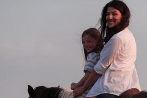 mãe e filha gostam de andar a cavalo juntos à beira-mar. foco seletivo foto