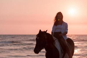 mulher com roupas de verão gosta de andar a cavalo em uma bela praia ao pôr do sol. foco seletivo foto