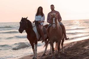 um casal apaixonado em roupas de verão, montando um cavalo em uma praia ao pôr do sol. mar e pôr do sol ao fundo. foco seletivo foto