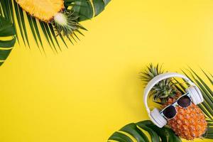 abacaxi engraçado usando fone de ouvido branco, ouça música, isolada em fundo amarelo com folhas de palmeira tropicais, vista superior, conceito de design plano leigo. foto