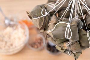 fabricação de zongzi de bolinho de arroz - envolvendo zongzi de bolinho de arroz chinês na mesa em casa para a celebração do festival do barco dragão, close-up, estilo de vida. foto