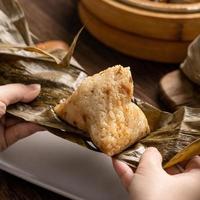 comendo zongzi - bolinho de arroz do festival do barco dragão jovem asiática comendo comida tradicional chinesa na mesa de madeira em casa celebração, close-up foto
