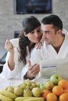 casal feliz lendo o jornal na cozinha no café da manhã foto