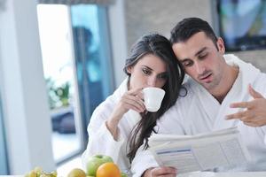 casal feliz lendo o jornal na cozinha no café da manhã foto