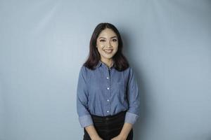 um retrato de uma mulher asiática feliz está sorrindo e vestindo uma camisa azul isolada por um fundo azul foto