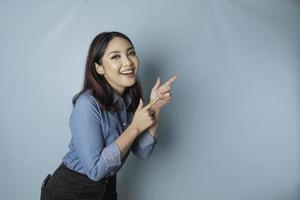 mulher asiática animada vestindo camisa azul apontando para o espaço de cópia ao lado dela, isolado por fundo azul foto