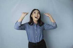 mulher asiática animada vestindo camisa azul apontando para o espaço de cópia para cima, isolado por fundo azul foto