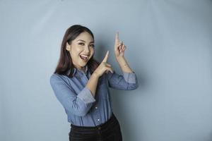 mulher asiática animada vestindo camisa azul apontando para o espaço de cópia ao lado dela, isolado por fundo azul foto