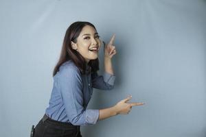 mulher asiática animada vestindo camisa azul apontando para o espaço de cópia ao lado dela, isolado por fundo azul foto