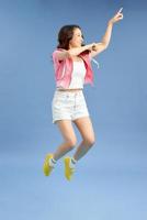 foto de senhora alegre asiática engraçada em t-shirt branca e jeans curtos pulando e sorrindo isolado sobre fundo azul.