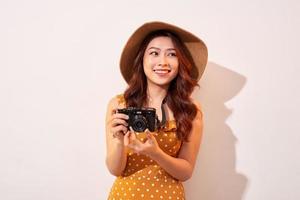 retrato de jovem sorridente alegre tirando foto com inspiração e usando vestido de verão. garota segurando a câmera retro. modelo posando em fundo bege com chapéu